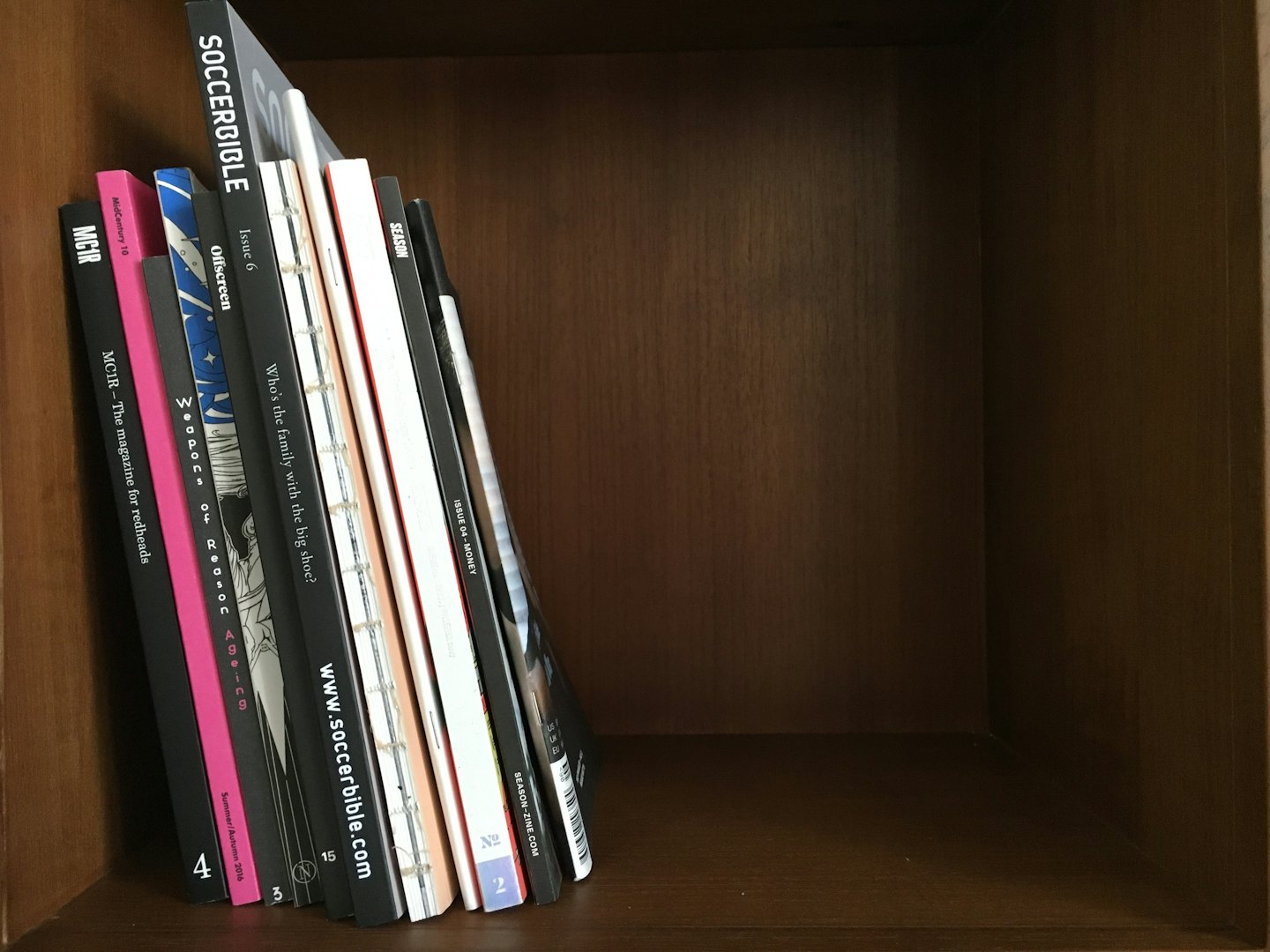 Ein Stapel verschiedener Zeitschriften und Zines in einem Holzregal.