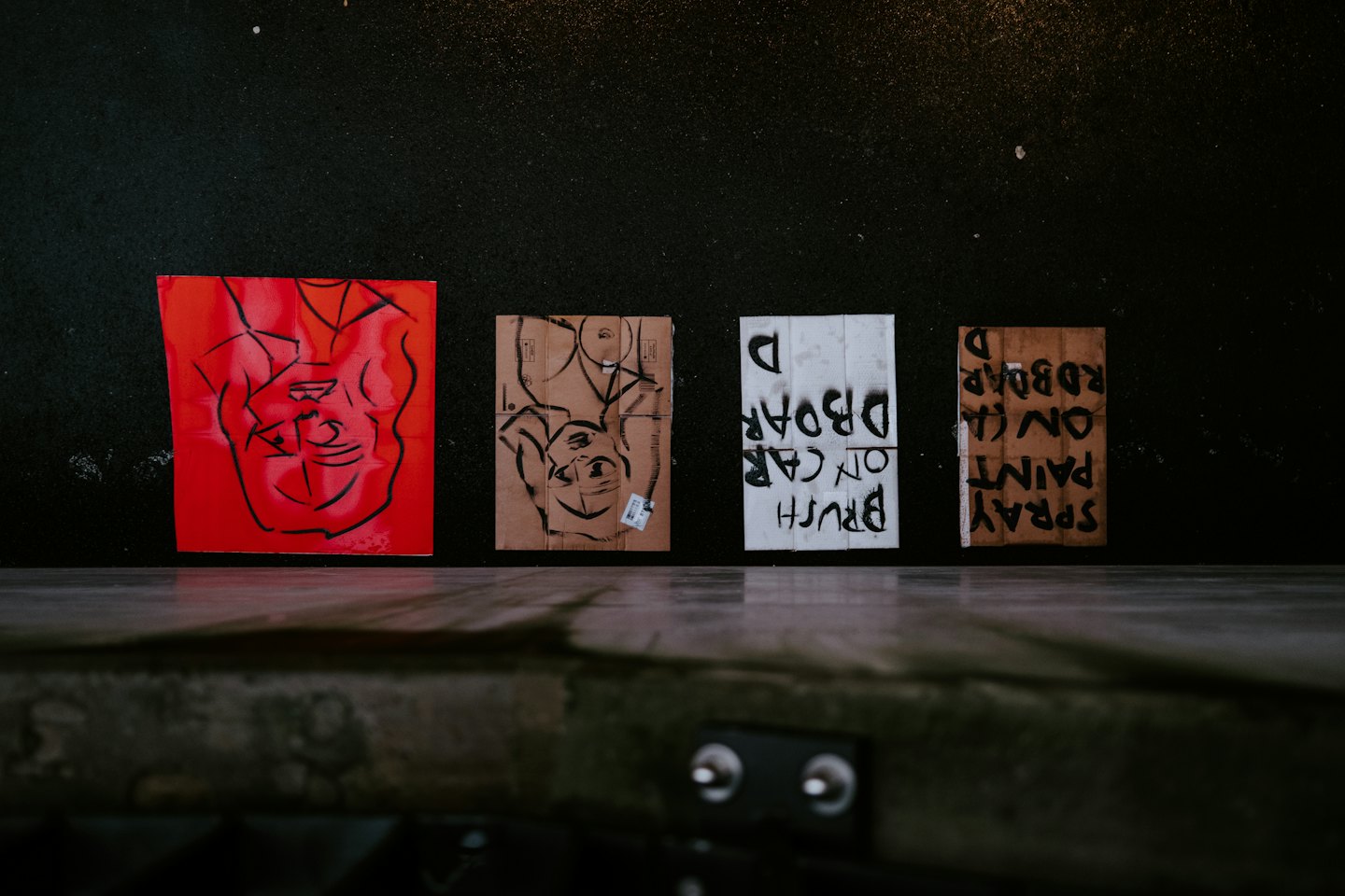 Vier Mixed-Media-Kunstwerke auf einem dunklen Boden arrangiert.