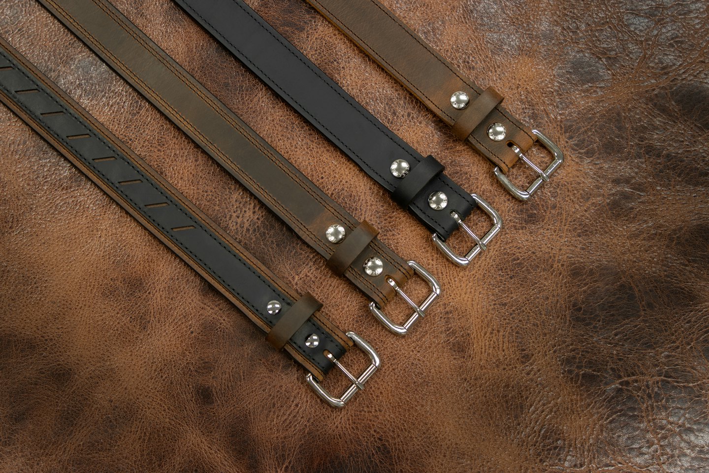 Vier braune und schwarze Ledergürtel mit silbernen Schnallen, diagonal angeordnet.