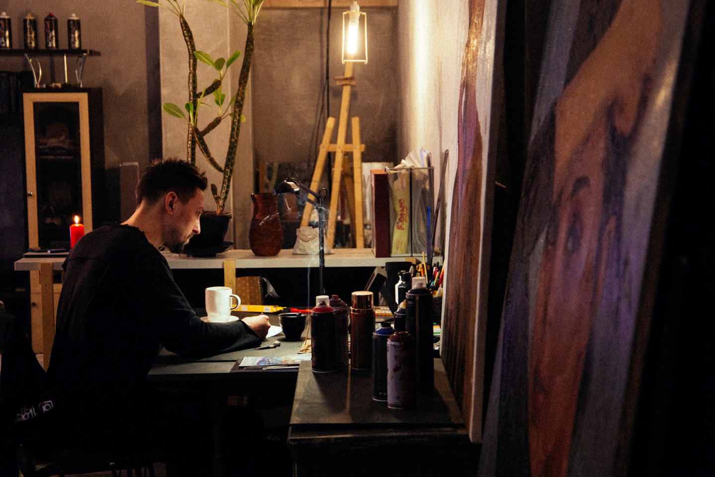 Mann, der an einem Schreibtisch voller Kunstbedarf skizziert.